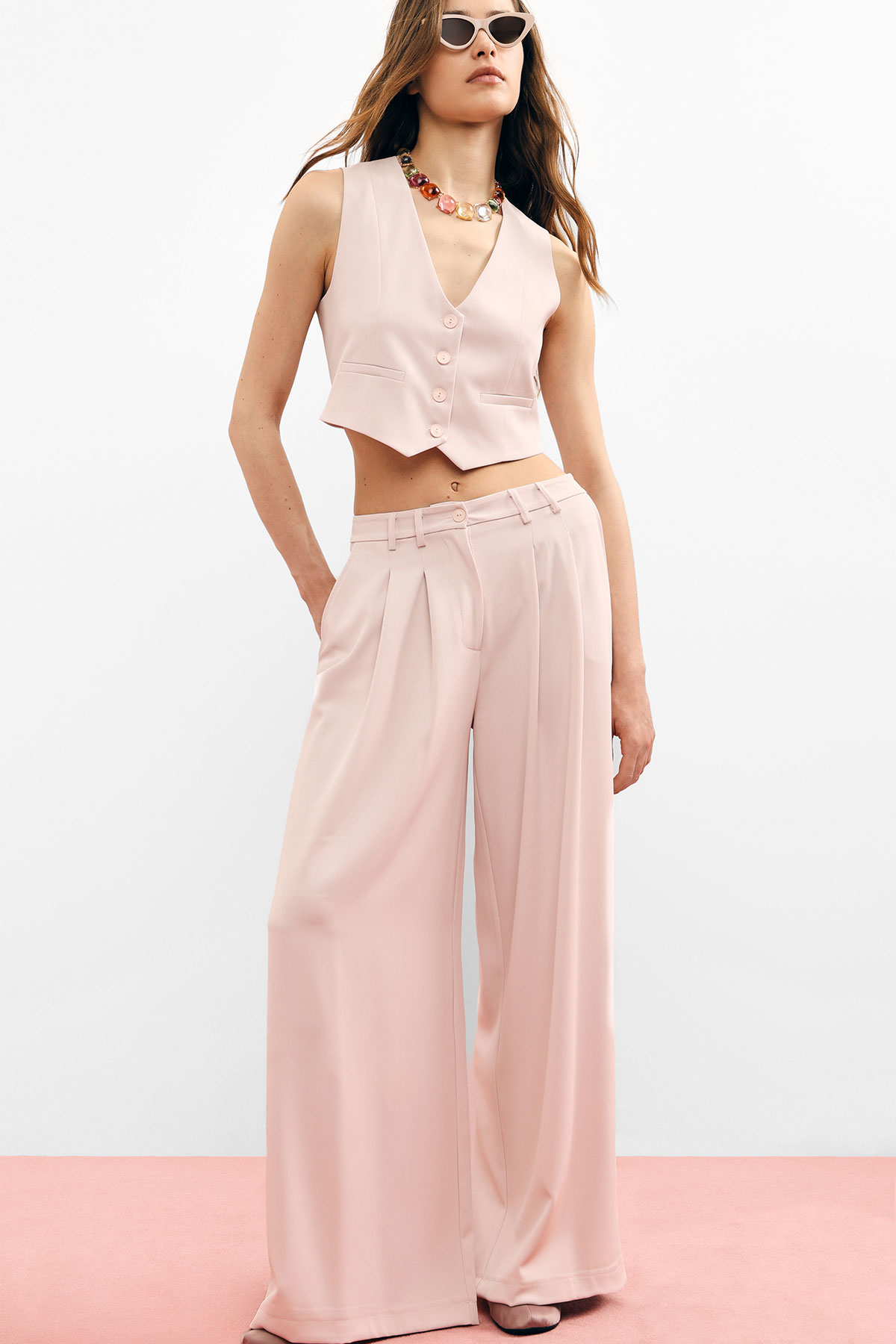 Model wearing pale pink cropped waistcoat and high-waist wide-leg trousers, sunglasses and statement necklace