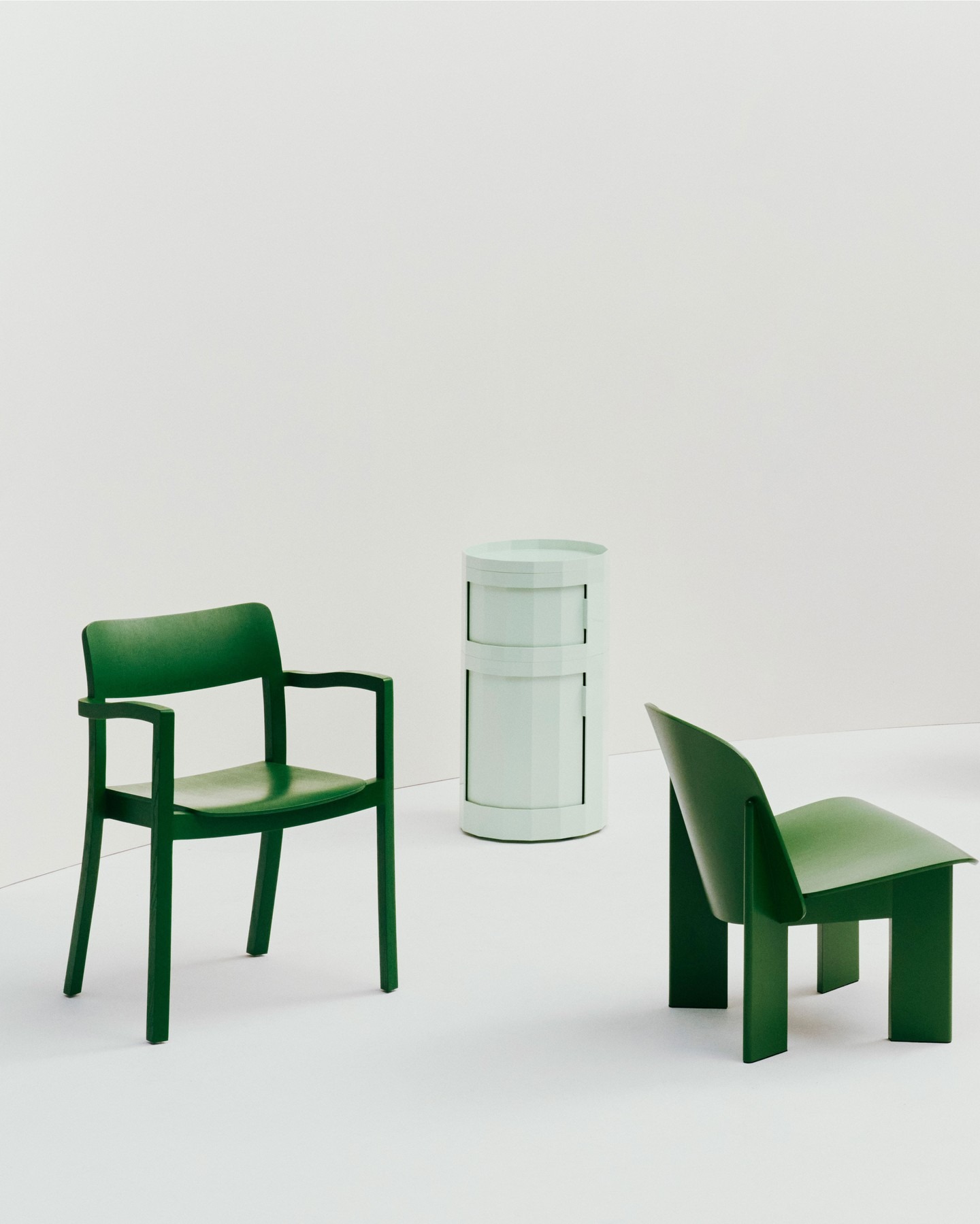 Minimalist studio scene with two green chairs and a pale green cylindrical side table on a white floor