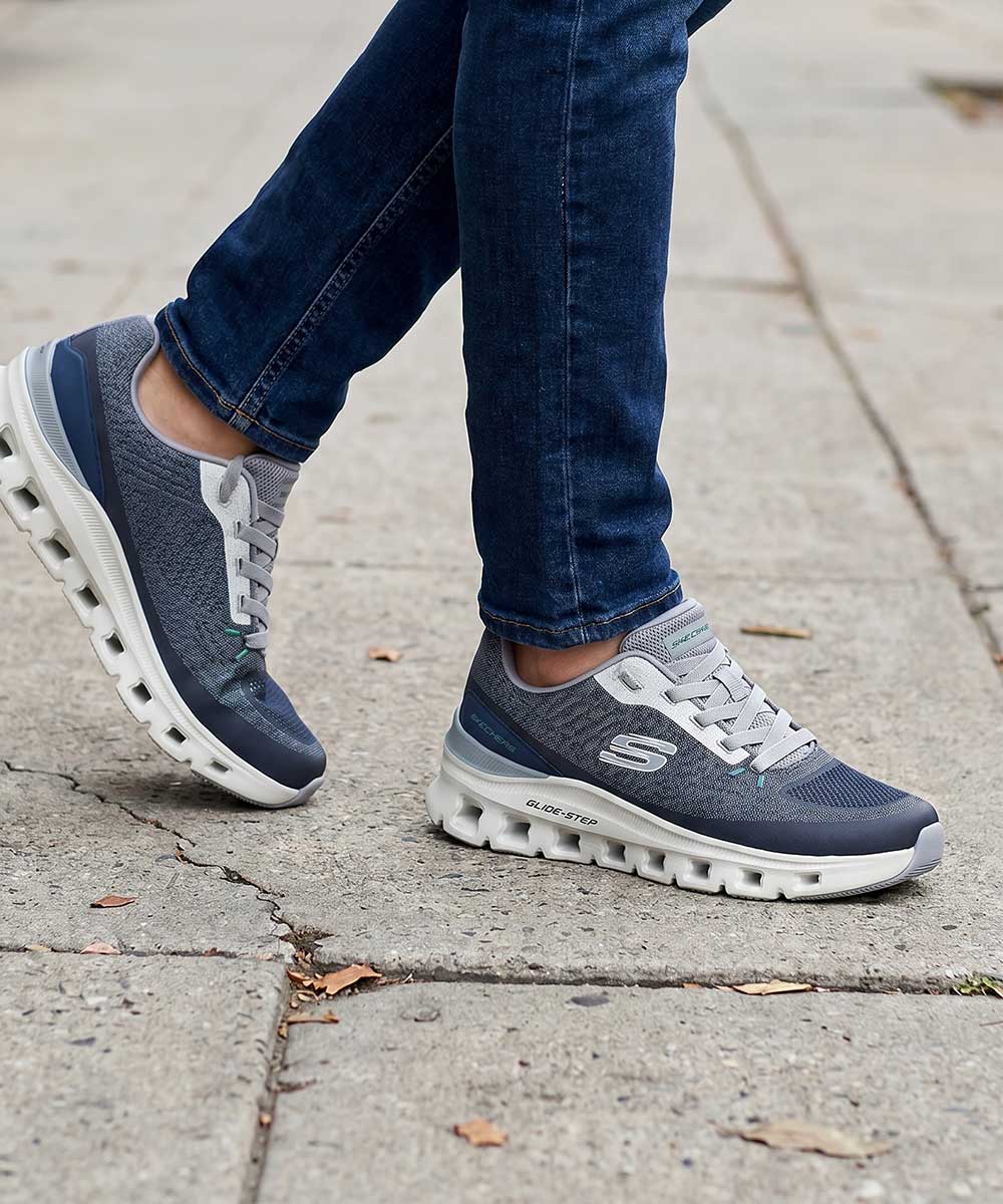 Grey Skechers Glide-Step sneakers on concrete pavement worn with slim blue jeans