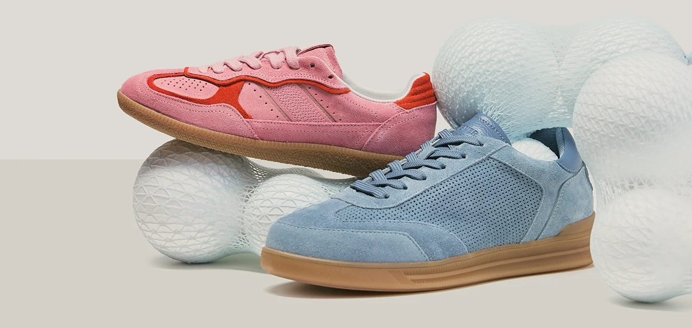 Scarpe da ginnastica in camoscio rosa e blu con suole in gomma, posizionate tra grandi sfere bianche testurizzate su uno sfondo neutro.