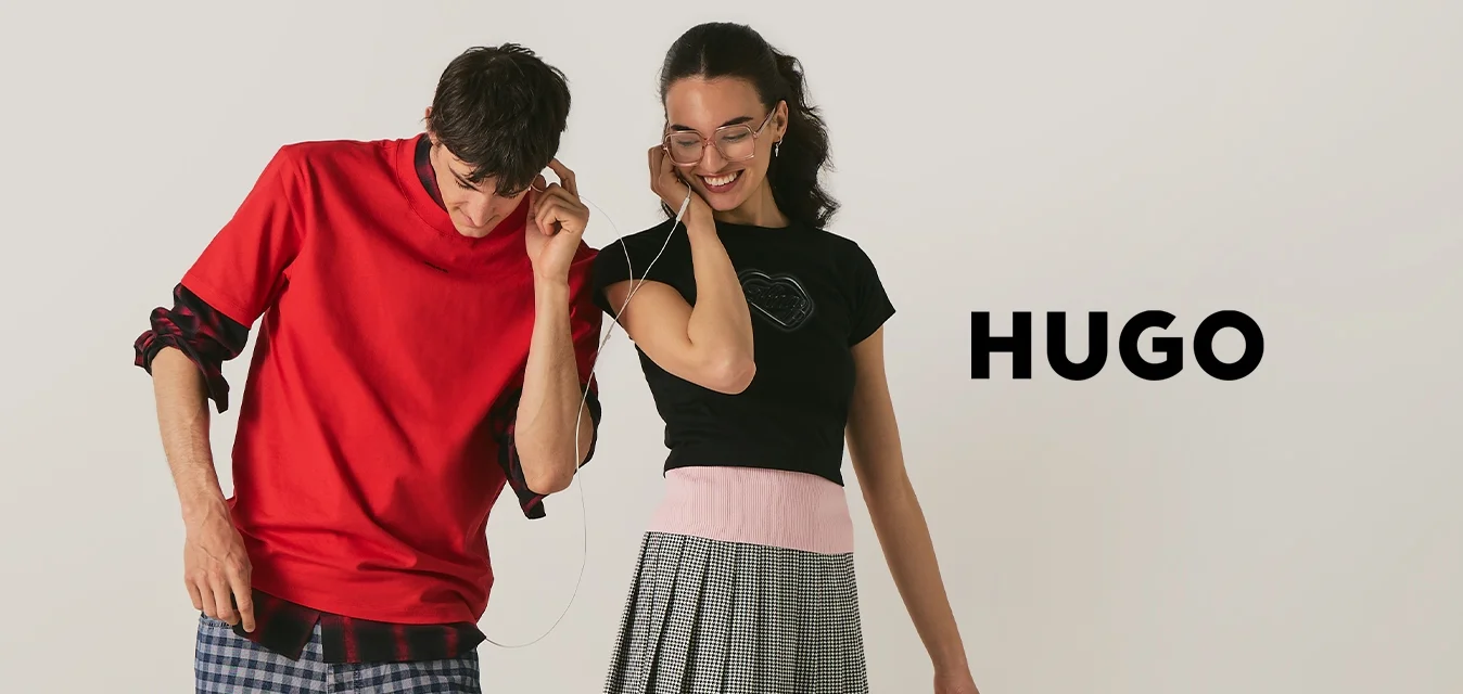 Ragazzo e ragazza adolescenti condividono le cuffie, stanno vicini, sorridono; lui indossa una camicia rossa e pantaloni a quadri, lei una canotta nera e una gonna grigia.