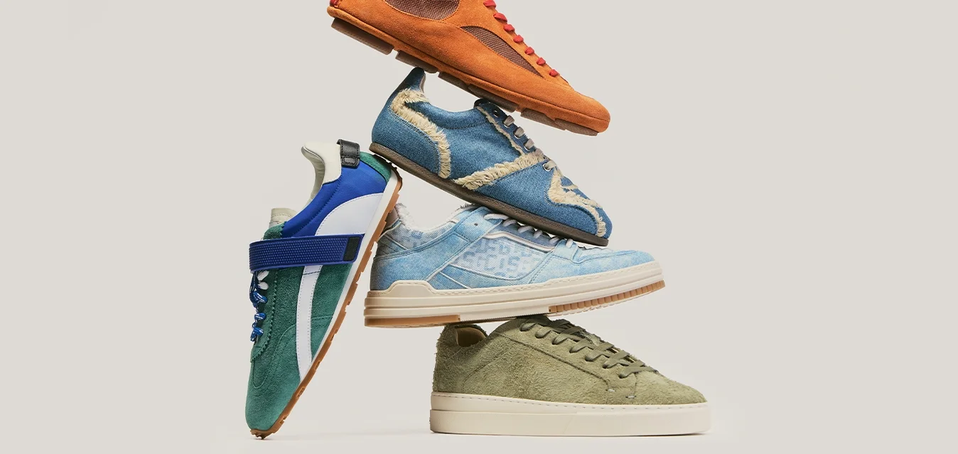 Stack di cinque sneaker casual arancioni, blu, verdi e in stile denim disposte su uno sfondo chiaro e semplice.