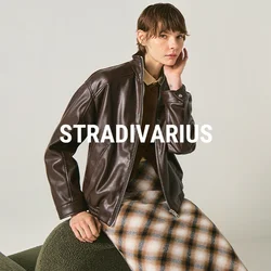 Persona con giacca di pelle marrone scuro e gonna a quadri, seduta su una sedia verde dalla texture evidente contro uno sfondo chiaro uniforme.