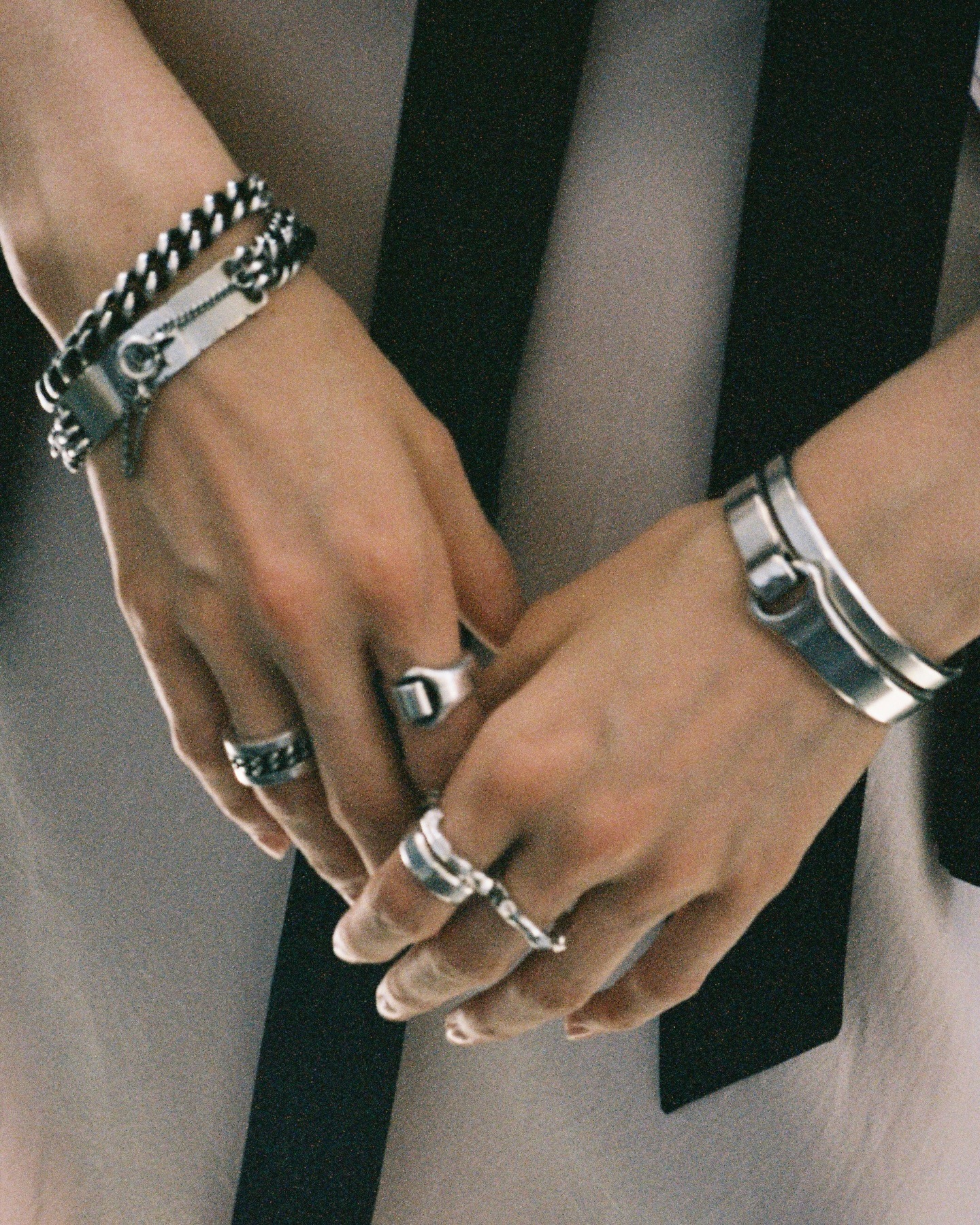 Close-up of hands wearing multiple silver rings and bracelets, intertwined fingers over black-and-white fabric, fashion jewellery detail