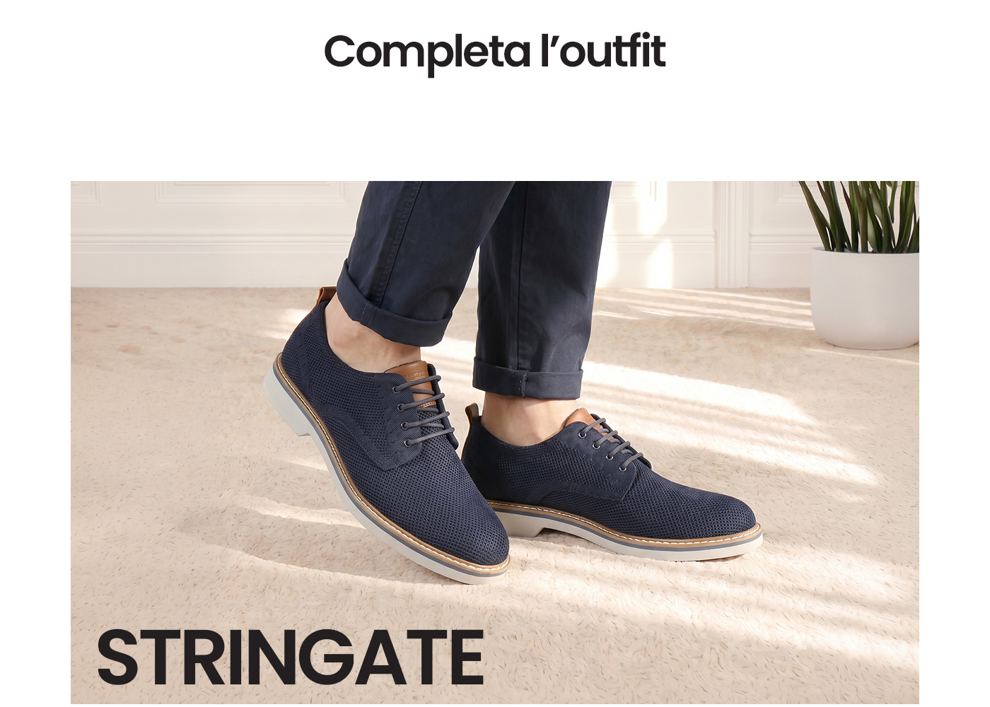 Navy knitted lace-up men's shoes on a cream carpet, model wearing rolled navy chinos in a bright indoor setting