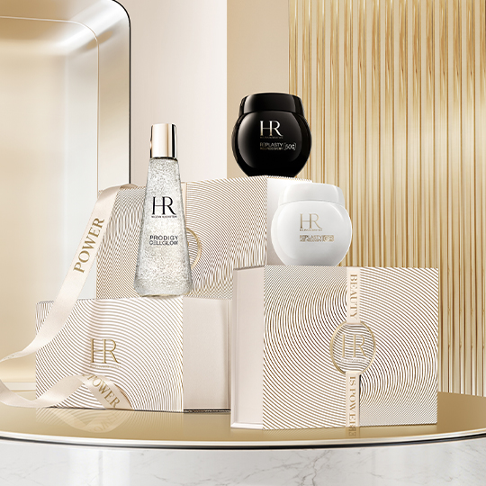 A hand reaches for the brand's two iconic creams, Age Recovery Night and Day, placed on a table with a golden trim.