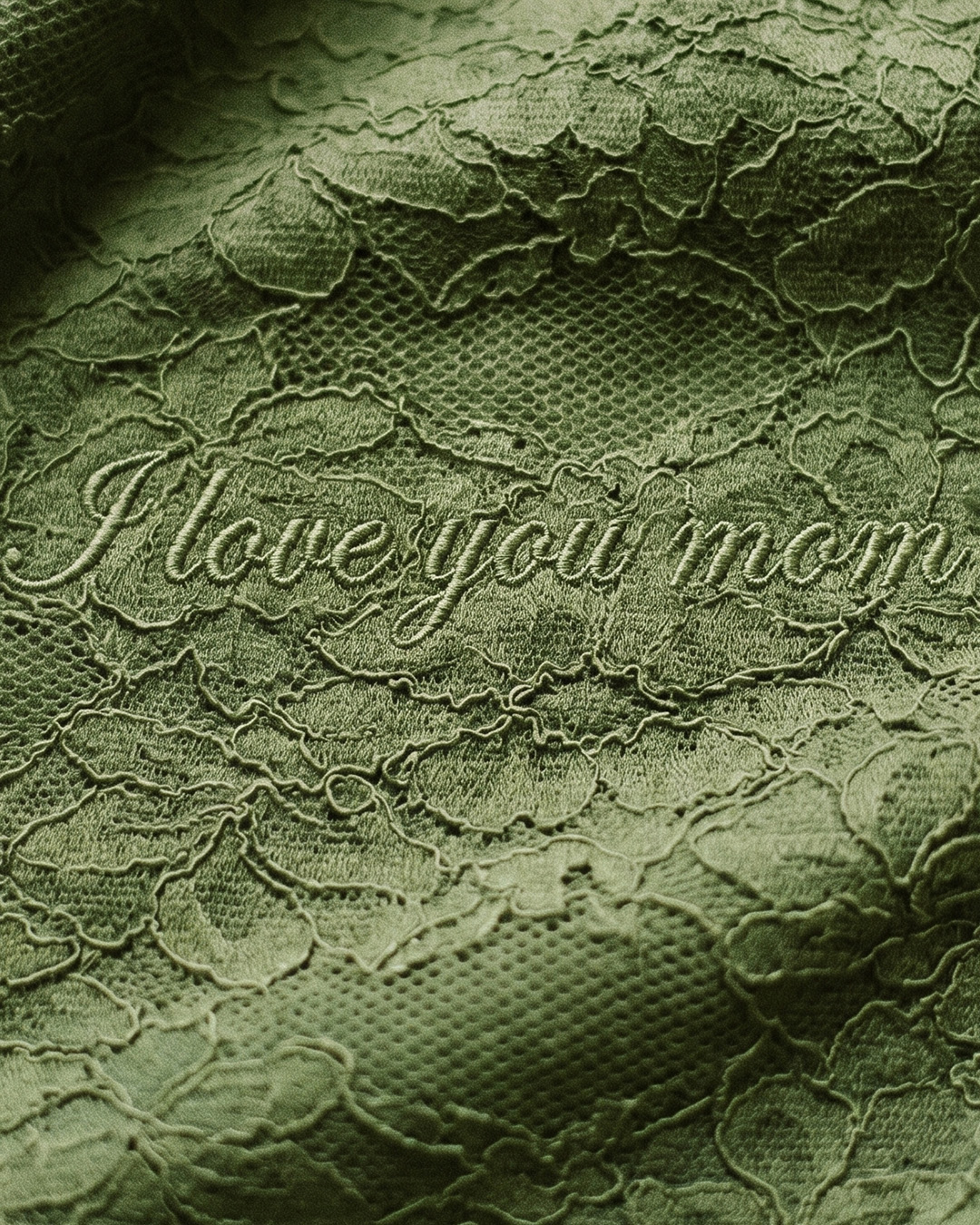 Close-up of green lace fabric with embroidered script reading 'I love you mom', showing delicate floral texture and stitching