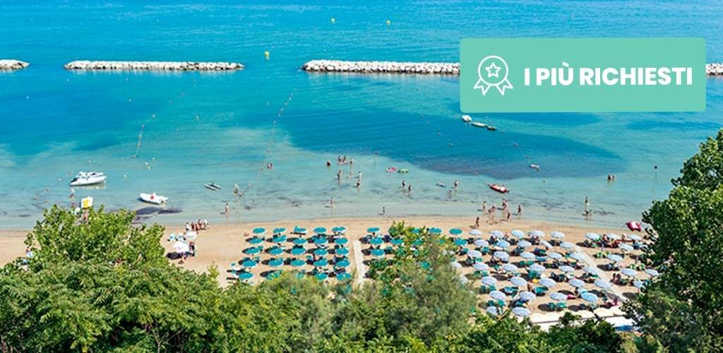 Aerial view of a sunny Mediterranean beach with turquoise sea, breakwaters, boats, rows of colourful beach umbrellas and swimmers