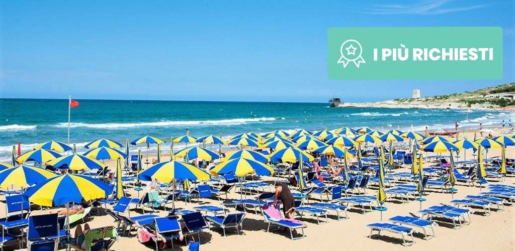Crowded sandy beach with rows of blue-and-yellow umbrellas and sunbeds by a turquoise sea, people relaxing under the sun