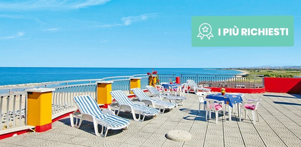 Seafront rooftop terrace with striped sunloungers and tables overlooking turquoise sea and sandy coastline under a clear blue sky