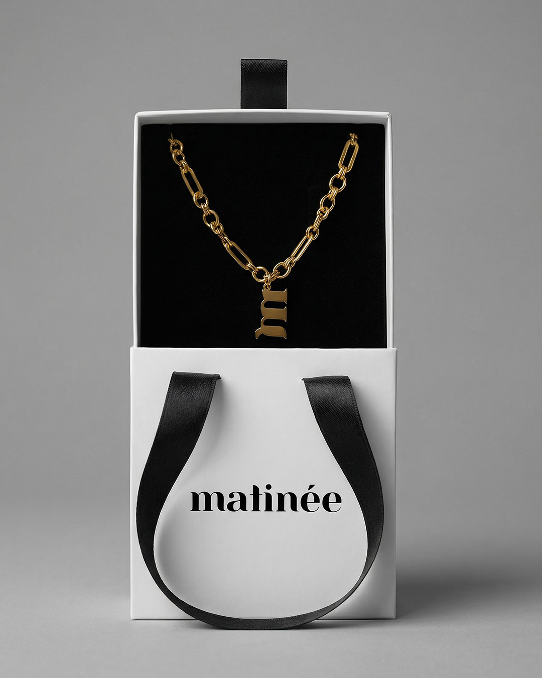 Gold chain necklace with lowercase 'm' pendant in white Matinée gift box with black velvet interior and black ribbon