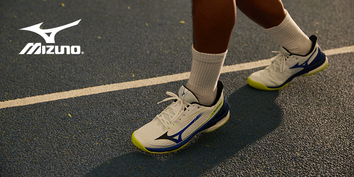 Close-up of white Mizuno running shoes with blue accents on a textured outdoor track, person wearing white socks