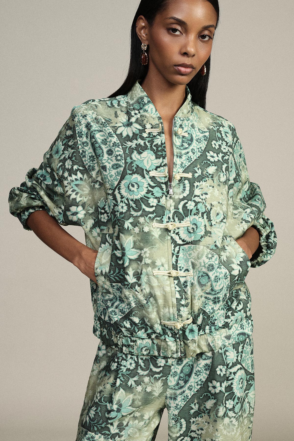 Model in green floral-print matching jacket and trousers with mandarin collar and frog closures, hands in pockets