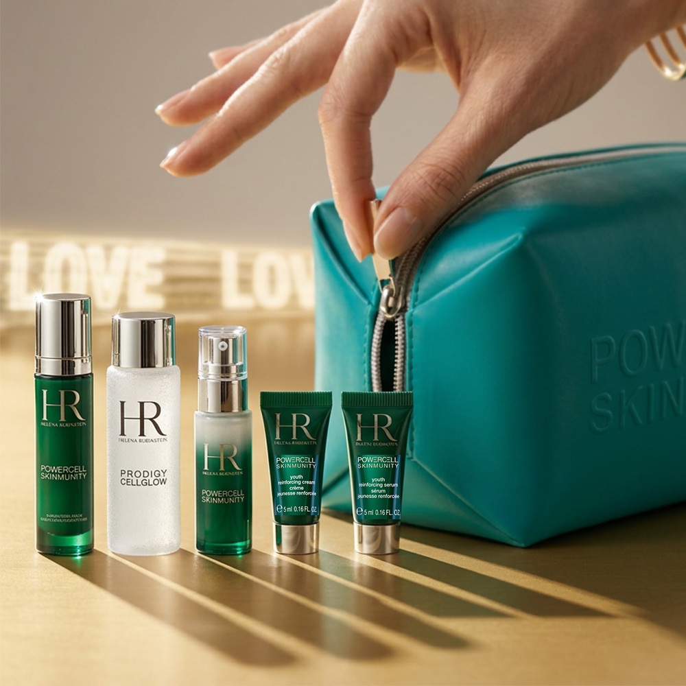 Una mano di donna apre la cerniera di un'elegante trousse verde ottanio. Accanto, cinque prodotti skincare in miniatura Helena Rubinstein delle linee Powercell e Prodigy Cellglow sono allineati su una superficie dorata. La scena &egrave; avvolta da una luce calda con la scritta luminosa "LOVE" sfocata sullo sfondo.