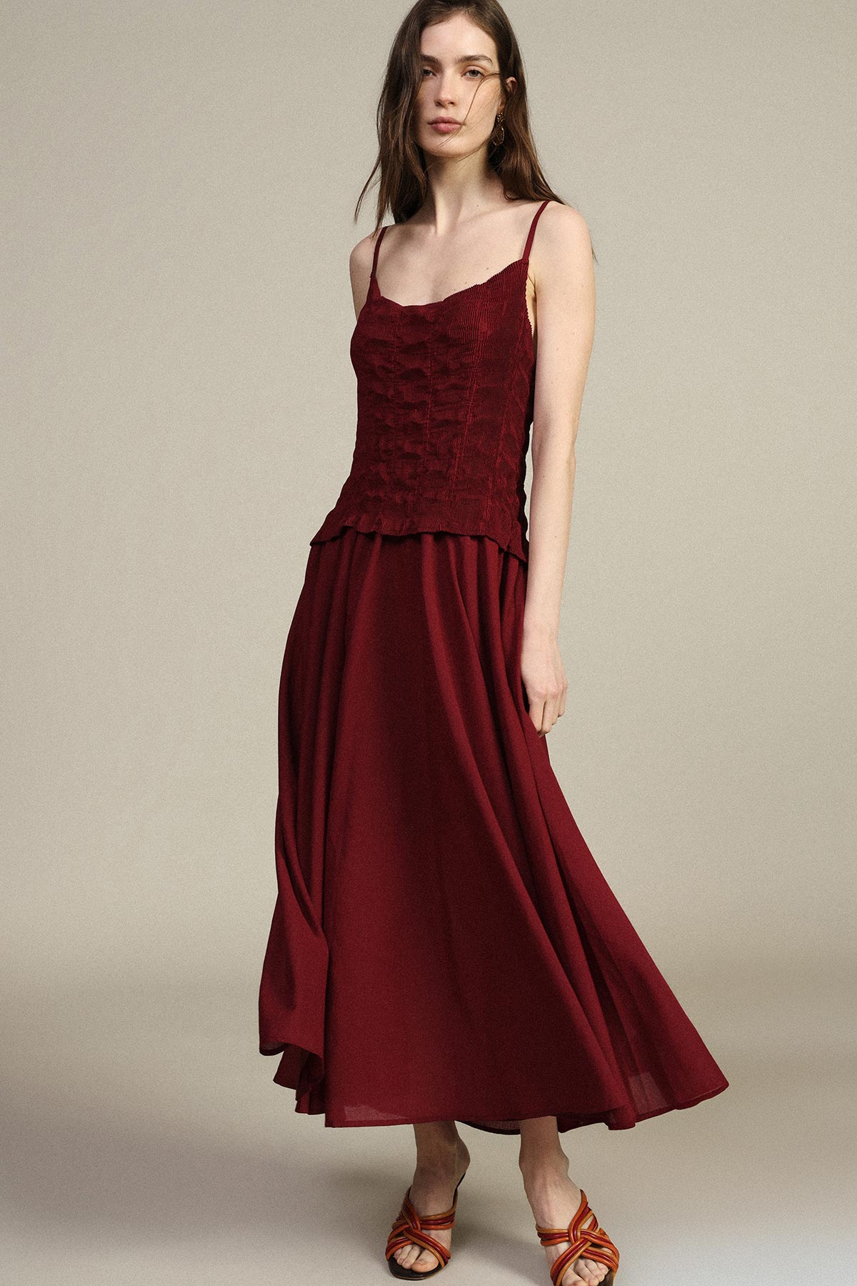 Woman in burgundy spaghetti-strap maxi dress with textured lace bodice and flowing skirt, wearing strappy sandals