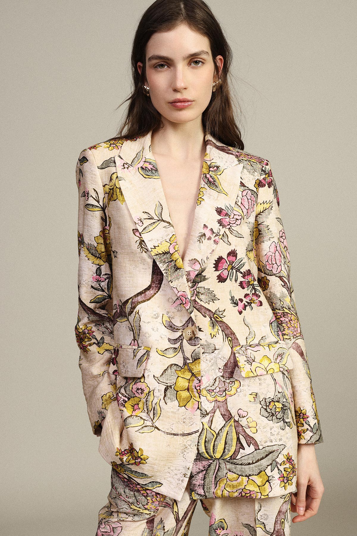 Woman wearing a pastel floral tailored blazer and matching trousers, hands in pockets against a neutral background