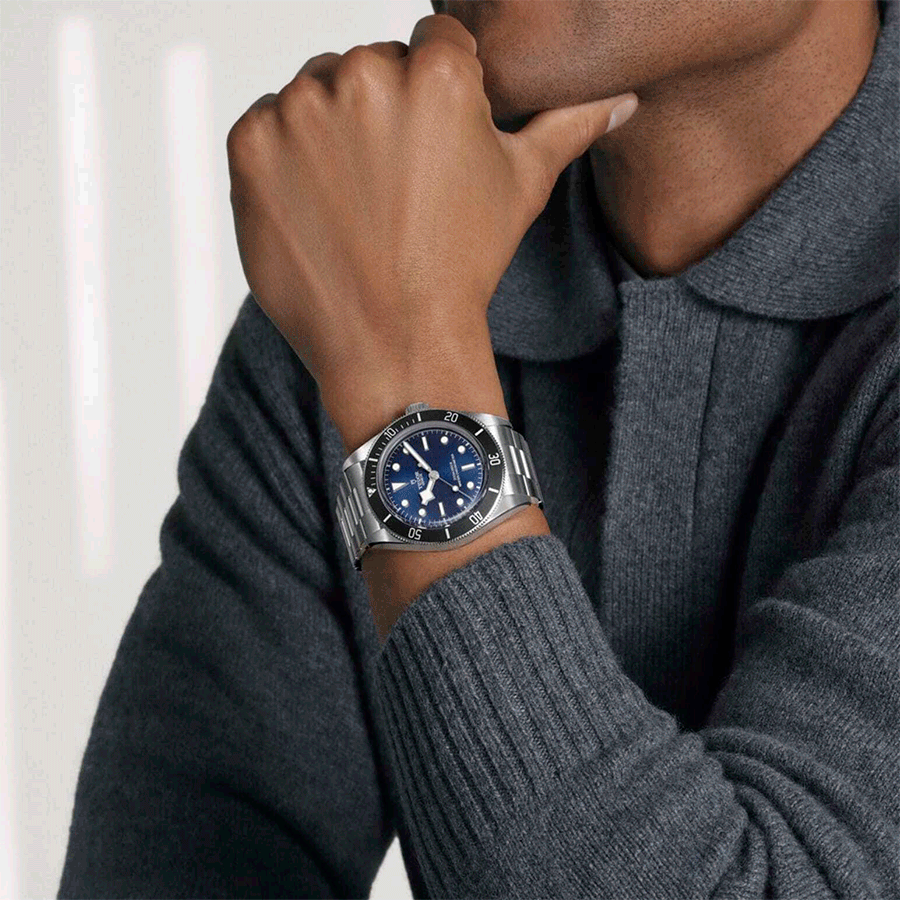 Collage of stainless steel men's wristwatches with blue and silver dials, shown on wrists and laid out alongside watchmaking tools