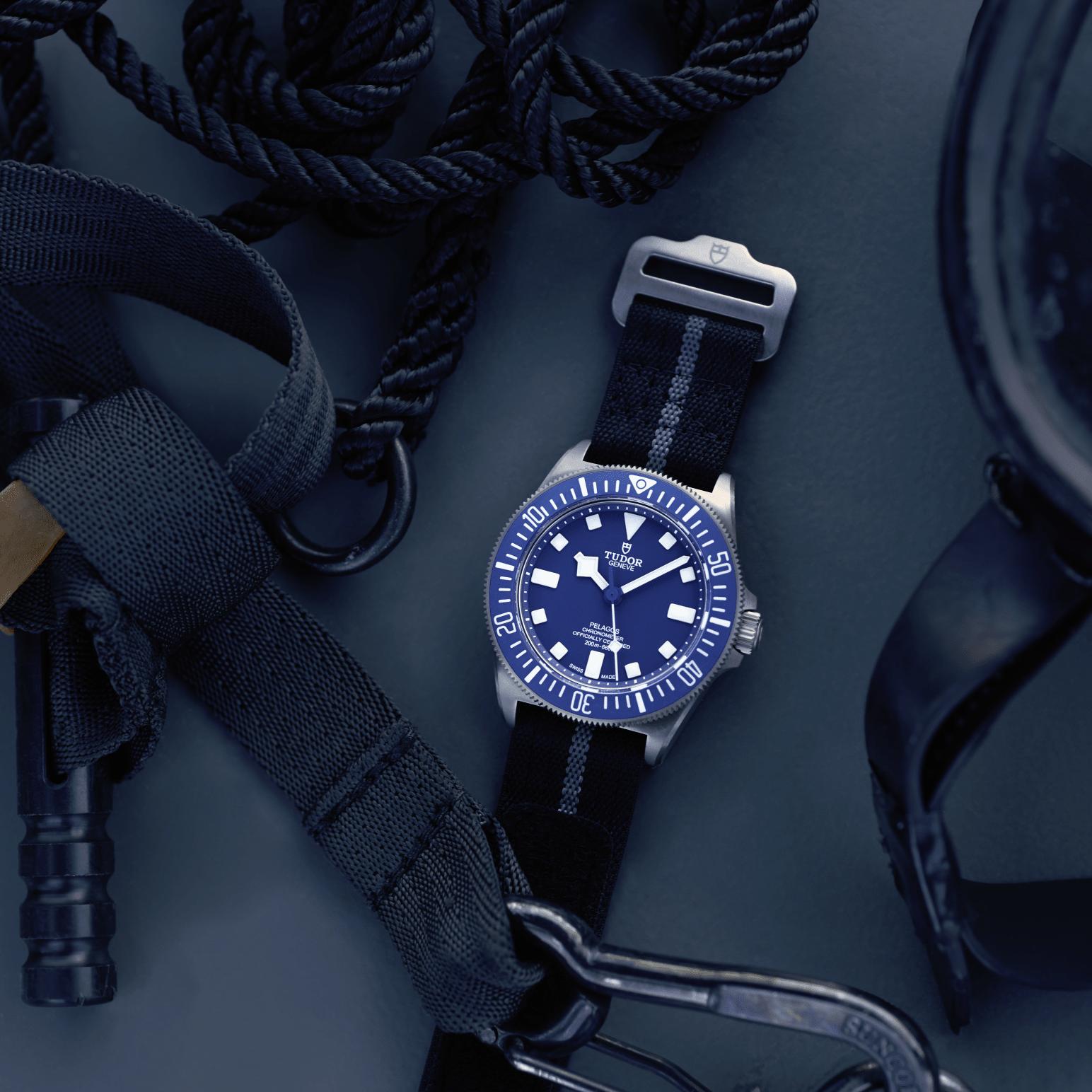 Blue dive watch with rotating bezel and black nylon strap placed among coiled rope and diving gear on a dark surface