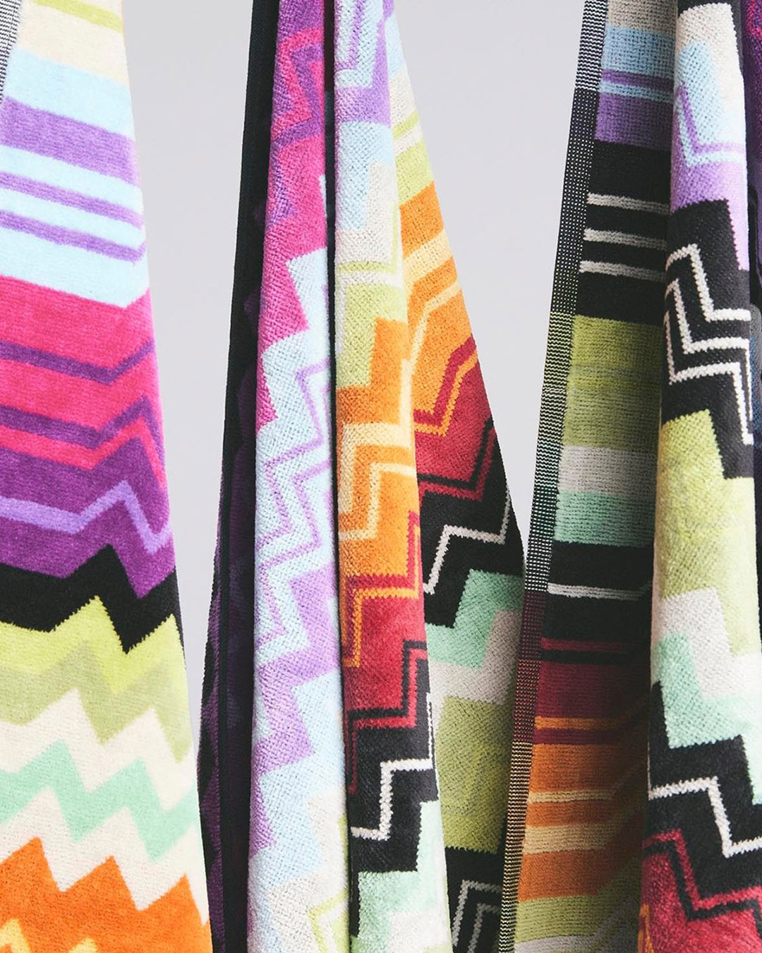 Colourful zigzag-patterned cotton towels hanging, close-up of multicolour chevron stripes and textured weave