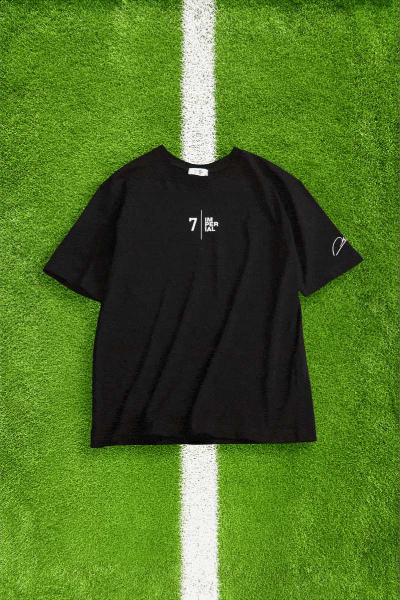 Flat-lay of nine assorted printed T-shirts on green artificial grass with white pitch lines, various colours and designs