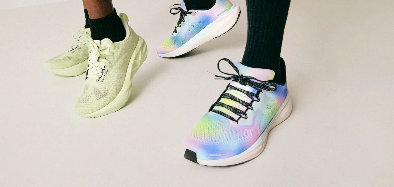 Due persone che indossano calze nere e scarpe da ginnastica colorate, in piedi su un pavimento chiaro contro uno sfondo uniforme.