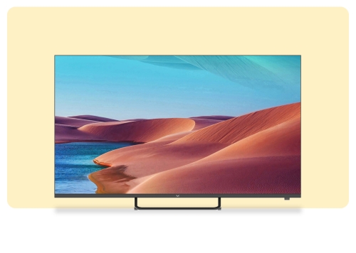Slim flat-screen TV on stand showing vivid desert dunes and turquoise water under a blue sky, set against a pale yellow backdrop