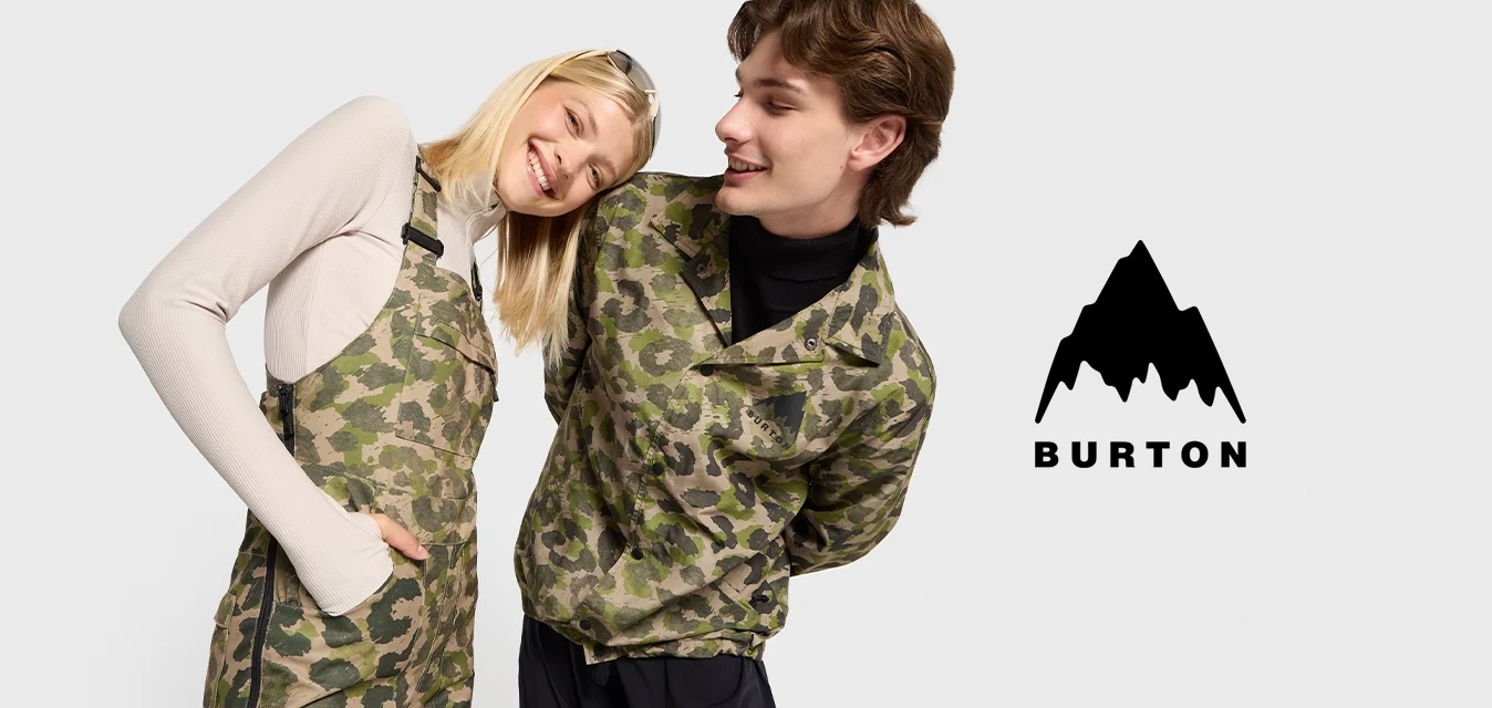 Due persone stanno vicine. Una indossa una giacca a motivo mimetico con pantaloni scuri; l'altra indossa una tuta beige sopra una maglietta a maniche lunghe.
