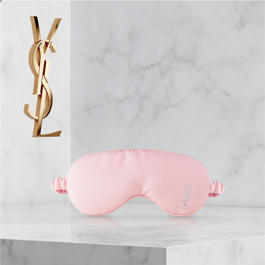 Una mascherina per dormire rosa YSL Beaut&eacute; su una superficie di marmo bianco.