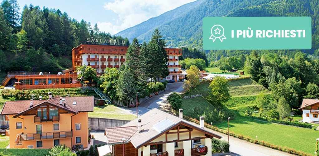 Alpine village with hotels and chalets beside green meadows and forested mountains under a blue sky