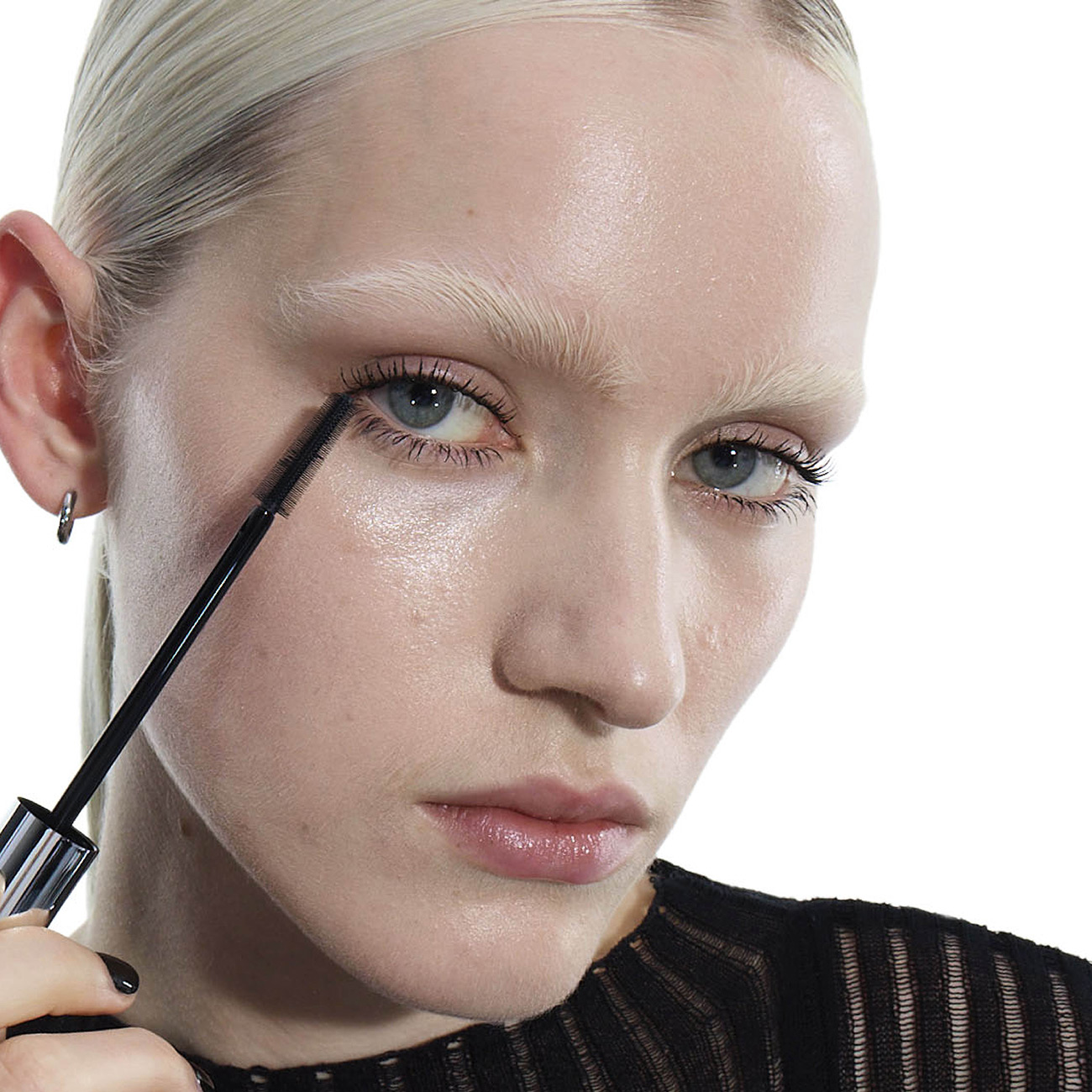 Una modella applica il mascara su uno sfondo bianco.