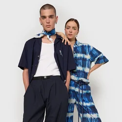 Due modelli posano insieme. Uno indossa una camicia blu scuro e pantaloni larghi; l'altro ha una tuta tie-dye blu. Entrambi hanno accessori minimal.