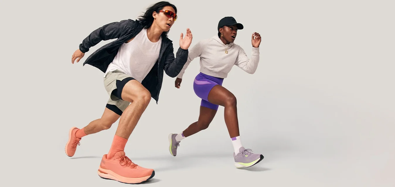 Due corridori, un uomo e una donna, che sprintano in avanti indossando abbigliamento sportivo e scarpe da ginnastica su uno sfondo chiaro e semplice.
