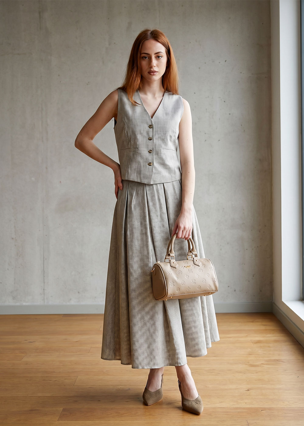 Young woman standing by a window in a grey checked sleeveless waistcoat and full skirt, holding a beige handbag