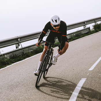 Cyclist in black racing kit and white helmet cornering on a road bike down a coastal bend, high speed, leaning into turn
