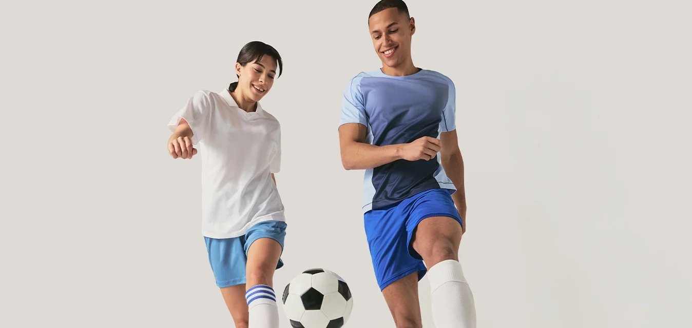 Due giovani con abbigliamento sportivo che calciare insieme un pallone da calcio su uno sfondo chiaro.