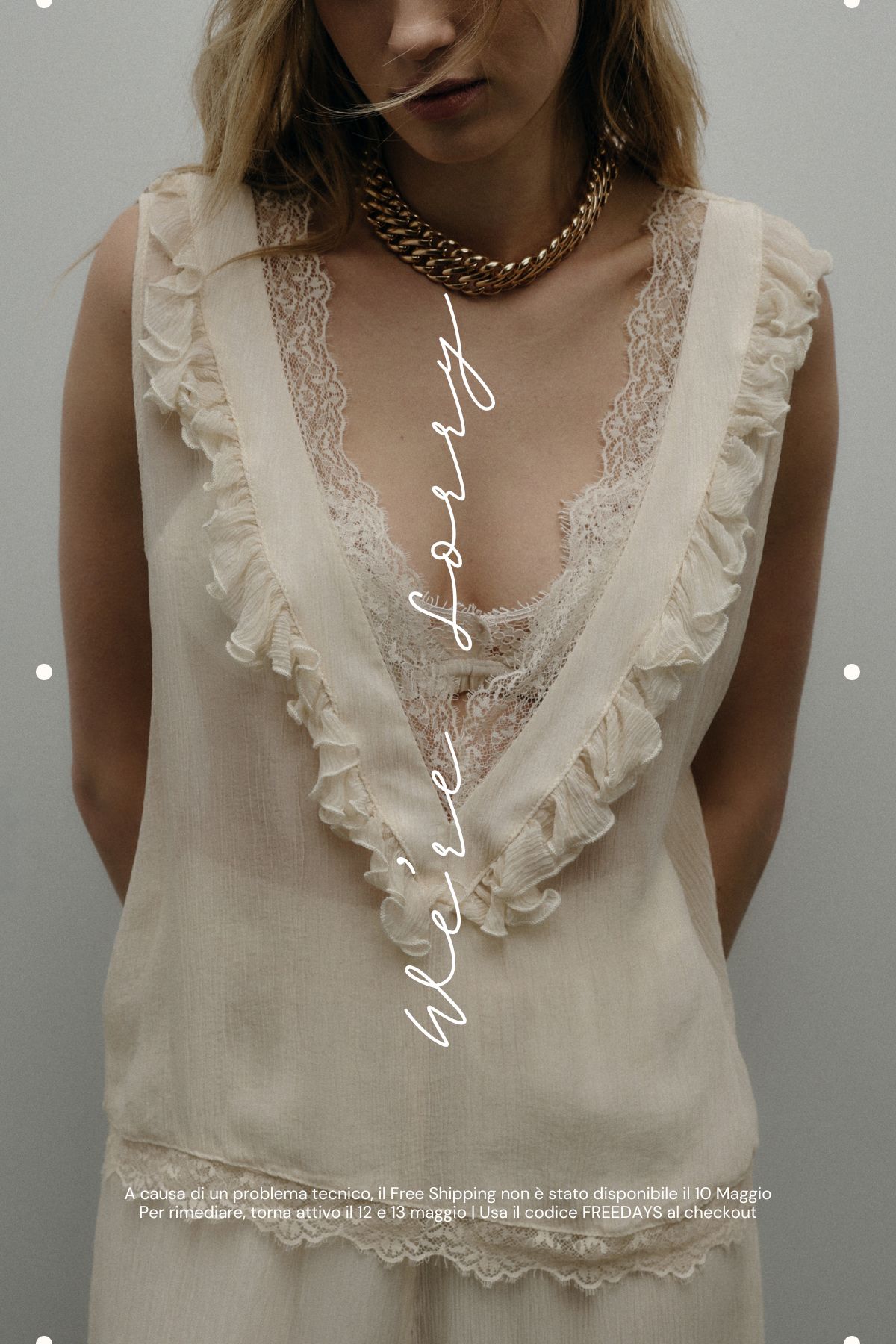 Model wearing cream lace-trimmed sleeveless blouse and chunky gold chain necklace against a neutral background