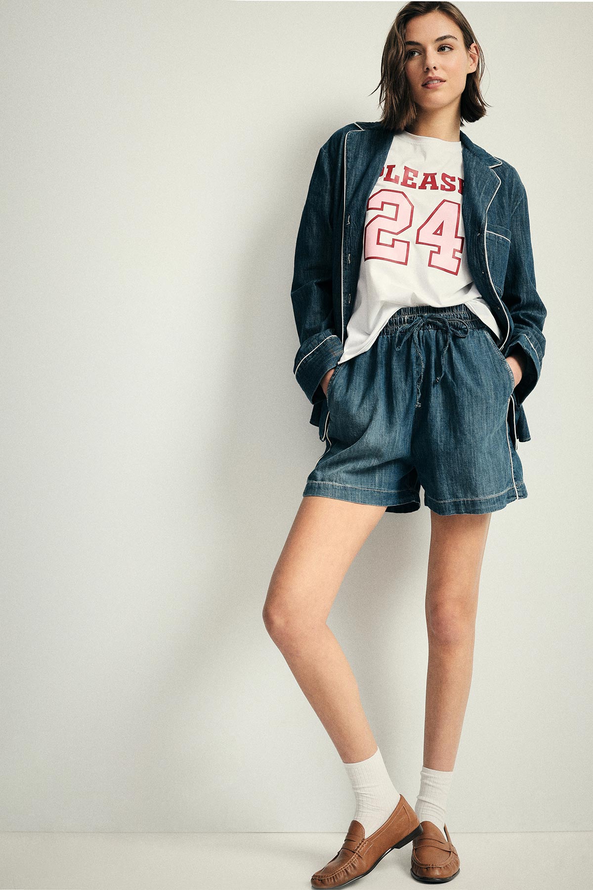 Young woman modelling denim blazer and drawstring shorts with white '24' T-shirt and brown loafers