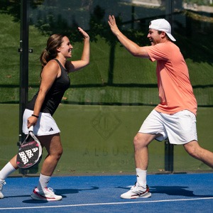 Two players high-fiving on a blue padel court, mixed-gender team in sportswear holding paddles, celebrating a point