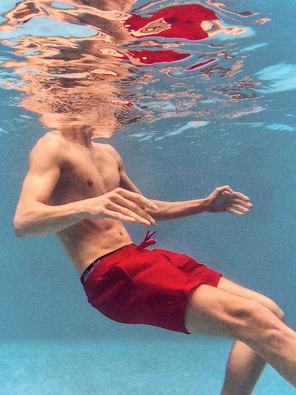 Modello con pantaloncini da bagno rossi sott’acqua.