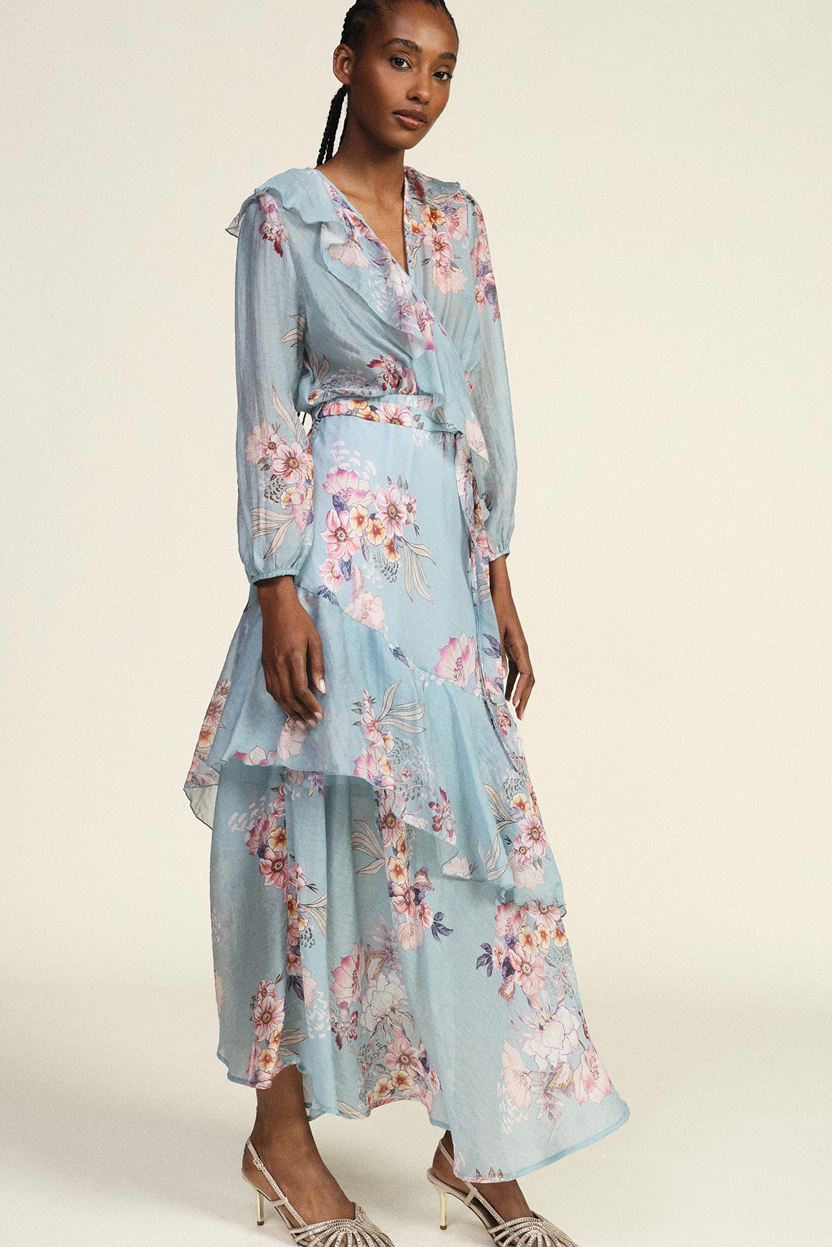 Woman wearing pastel blue floral wrap dress with ruffled tiers and long sleeves, paired with heeled sandals