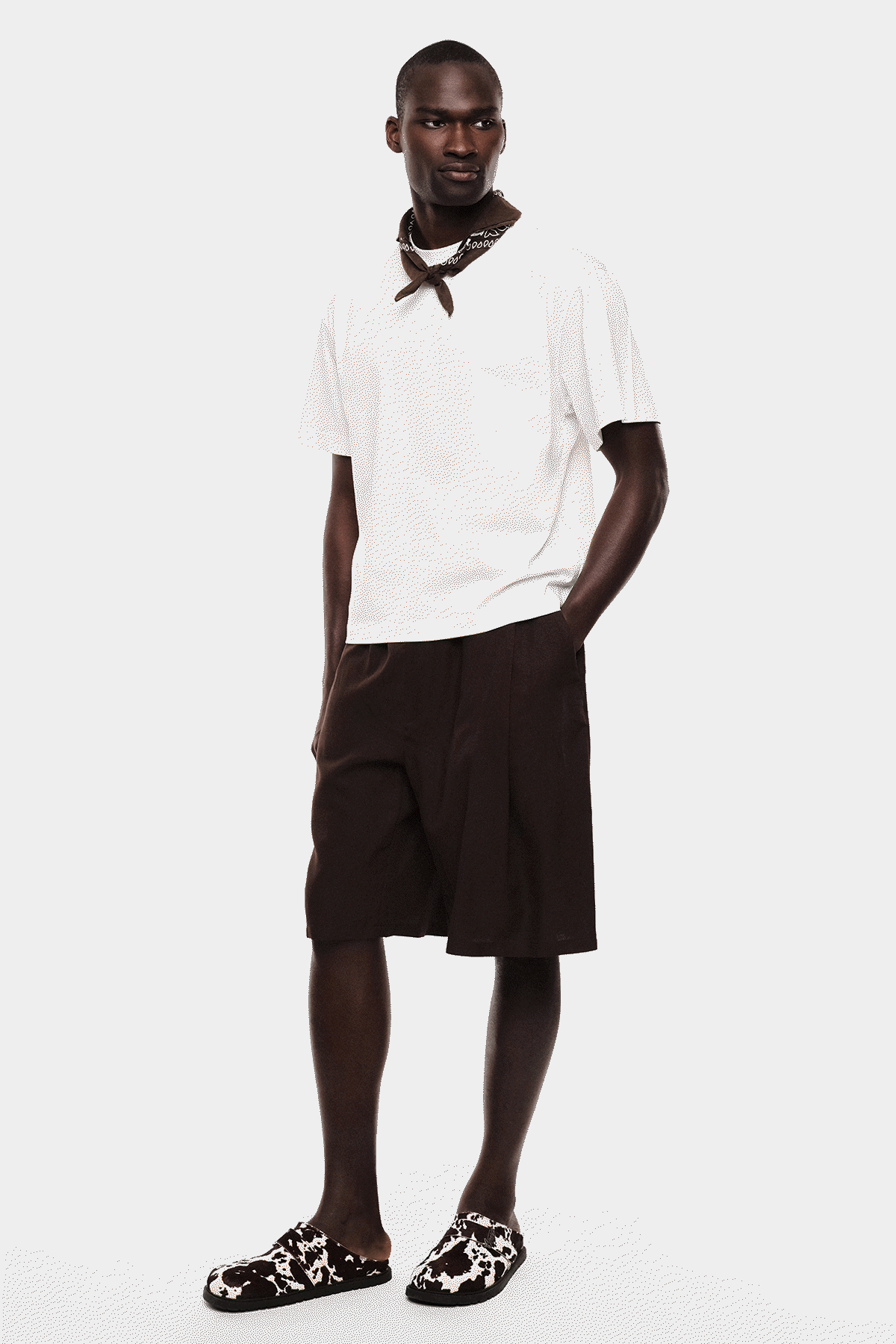 Collage of male model in a white polo, black knee-length shorts and patterned slip-on shoes, shown in multiple standing poses on a white background