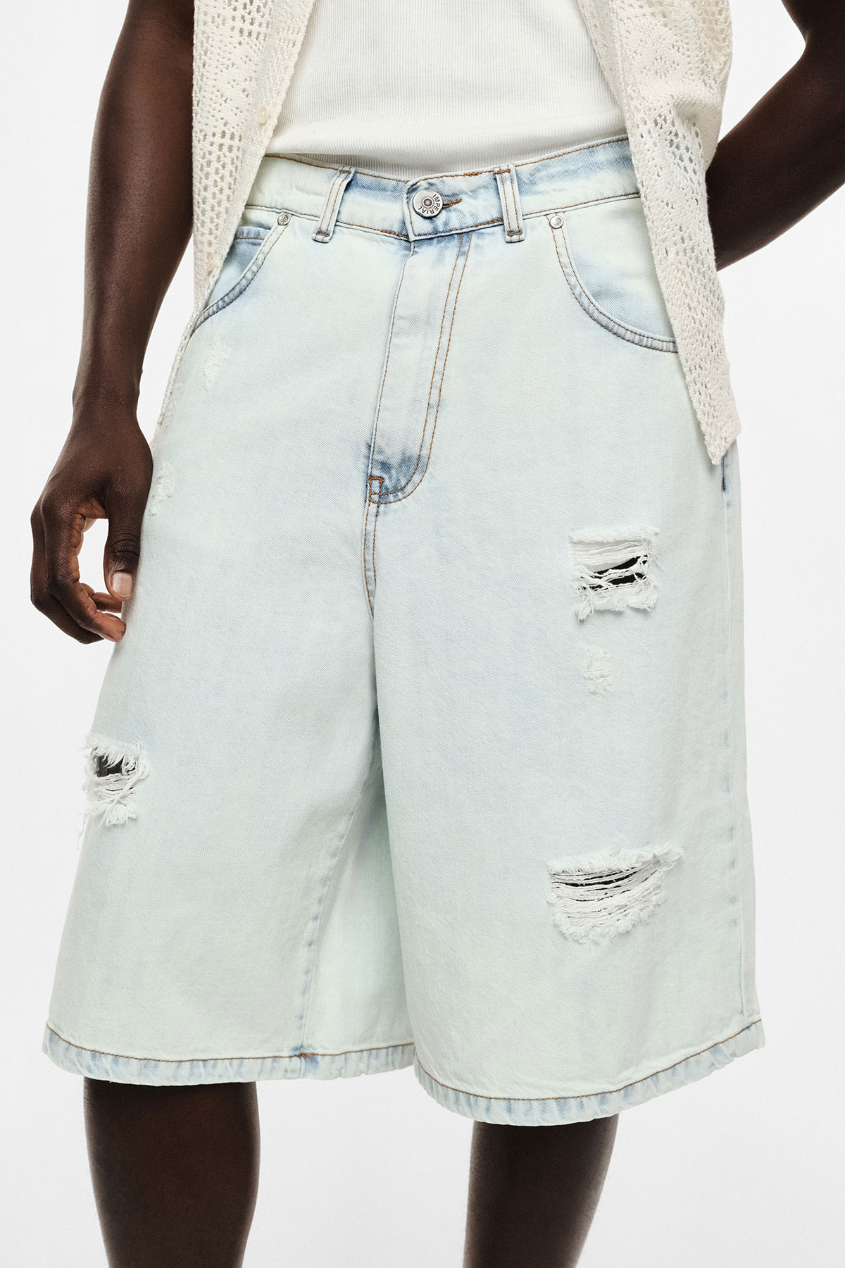 Light-wash distressed denim Bermuda shorts with knee-length relaxed fit, frayed ripped details and button waist on model