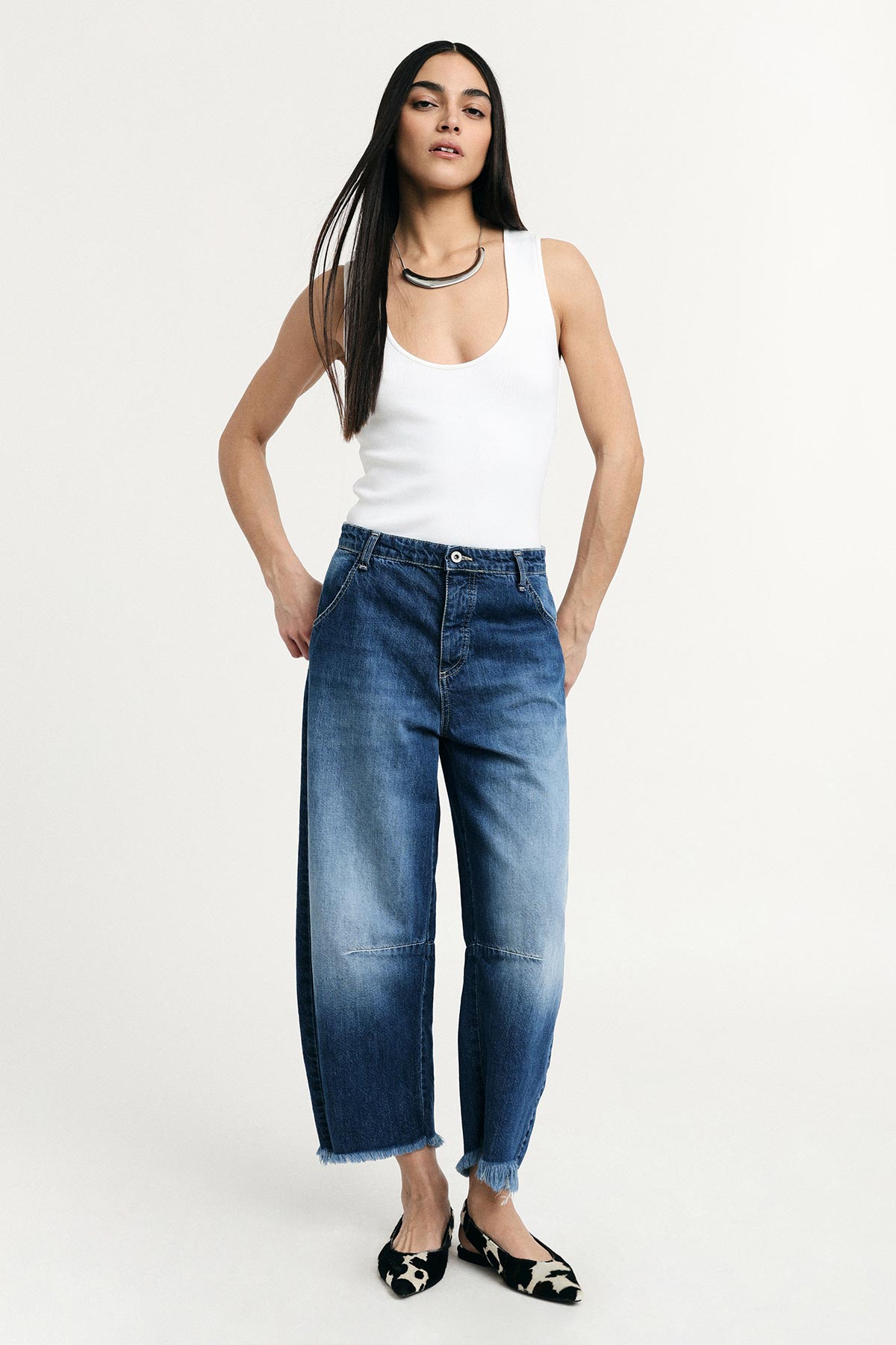 Model in white scoop-neck tank, high-waist cropped wide-leg blue jeans with frayed hems, silver necklace and patterned flats