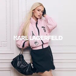 Donna con lunghi capelli biondi indossa una giacca rosa con toppe, una gonna nera, un guanto nero e tiene una borsa nera con tracolla a catena dorata.