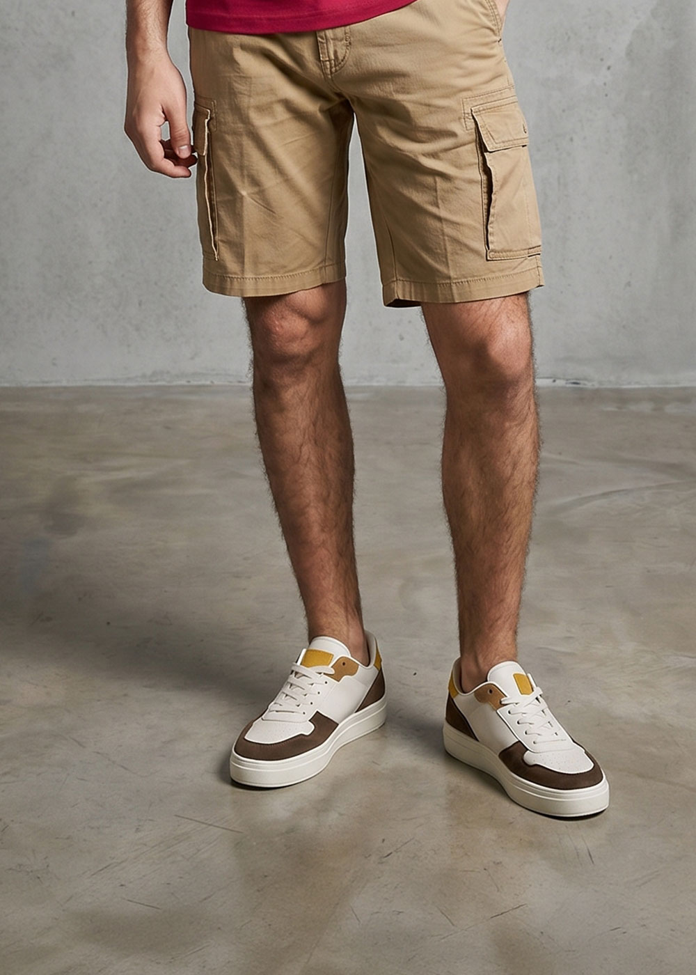 Male model's lower body wearing khaki cargo shorts and white-and-brown trainers standing on a concrete floor