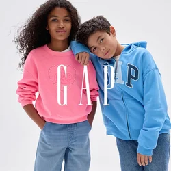 Due bambini stanno insieme; la ragazza con felpa rosa e jeans larghi, il ragazzo con felpa blu GAP e jeans appoggia la testa sulla spalla della ragazza.