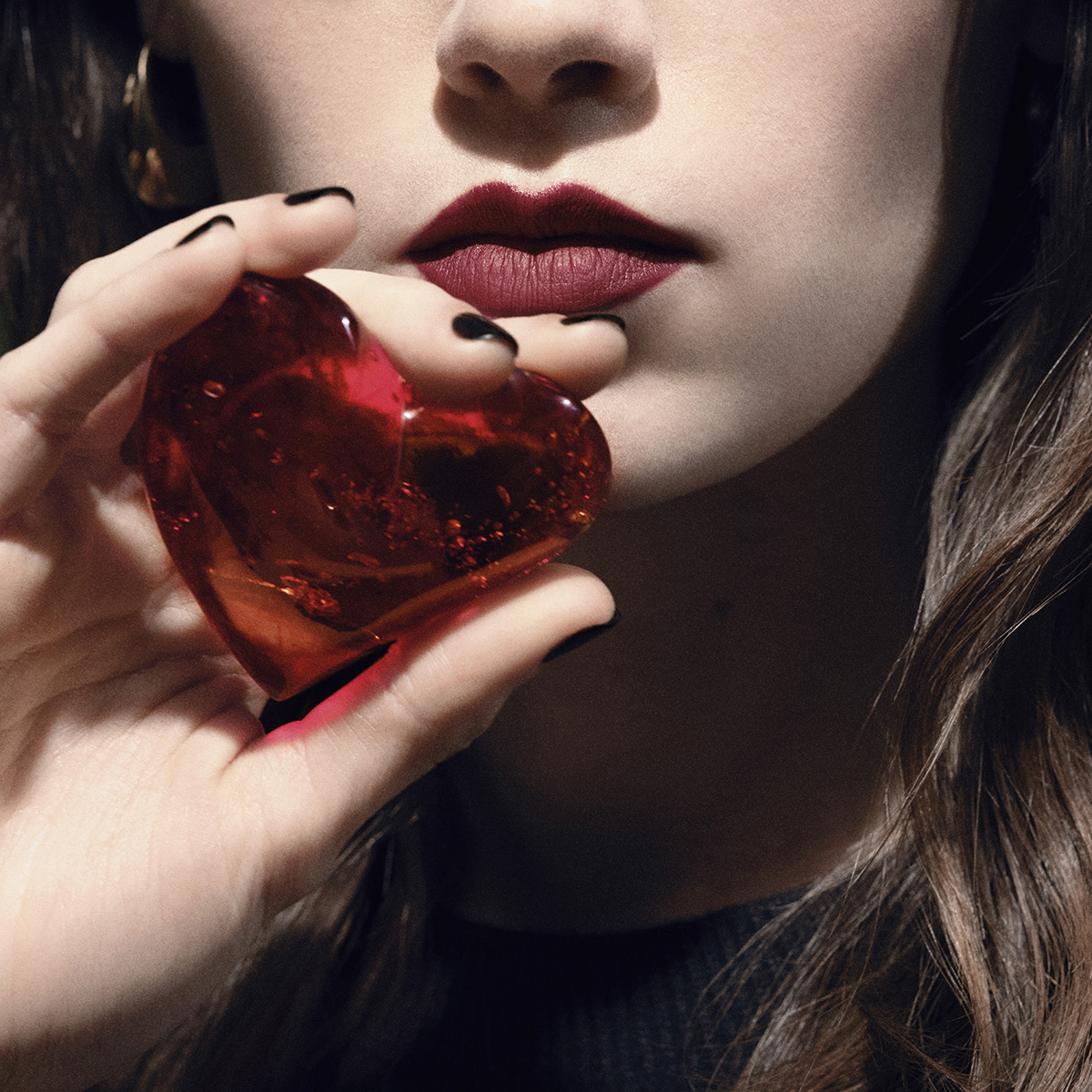 Una modella con rossetto rosso tiene un cuore di vetro rosso traslucido.