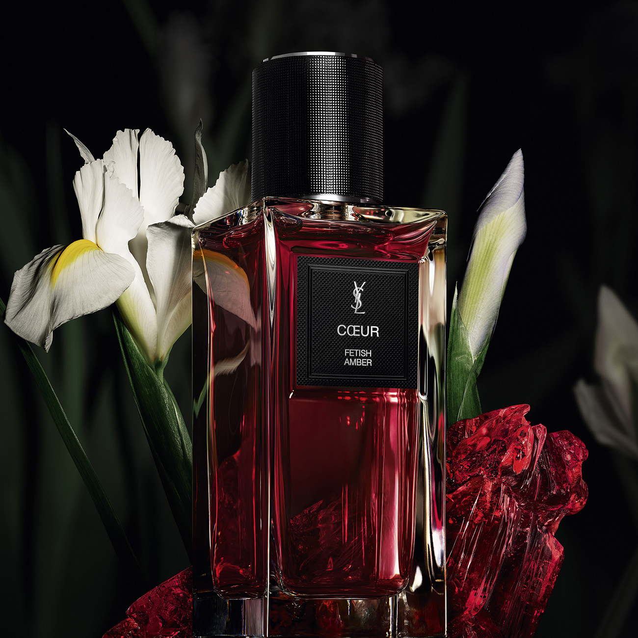 Flacone di profumo YSL C&oelig;ur Fetish Amber con fiori bianchi e cristalli rossi.