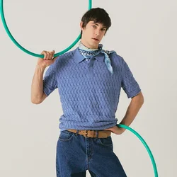 Persona con maglione blu e jeans posa con un hula hoop verde, in piedi davanti a uno sfondo chiaro e uniforme.