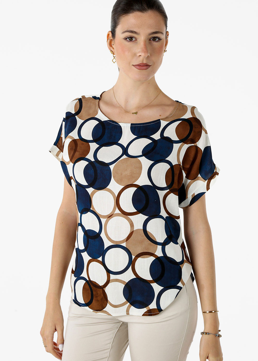 Woman modelling short-sleeve blouse with navy and brown circular print, cream trousers and minimal jewellery on white background